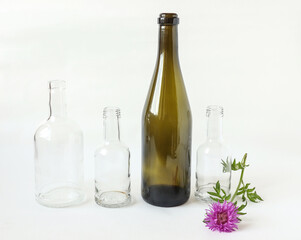 The concept of selective waste collection that reduces the carbon footprint : glass bottles of different sizes and colors with a flower on a white background, close-up, side view
