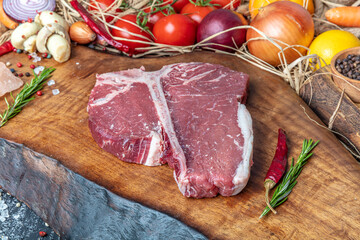 Raw t bone steak is on a wooden Board on black background, next to salt, pepper and herbs.