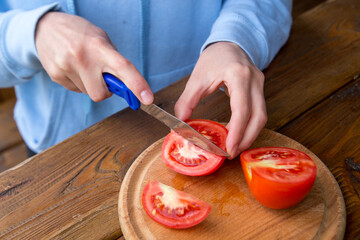 hands of a girl cut tomates on a wooden table, the process of making vegetarian salad, close-up...