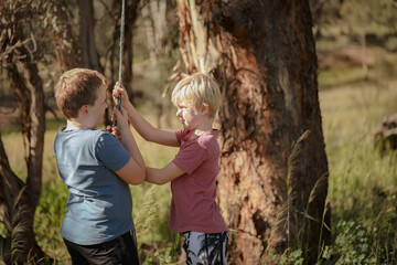Two brothers playing on rope swing in beautiful bush location. Outdoor play during times of self isolation using imagination.