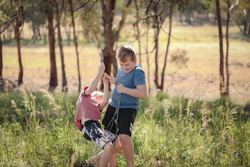 Two brothers playing on rope swing in beautiful bush location. Outdoor play during times of self isolation due to Covid 19 using imagination.