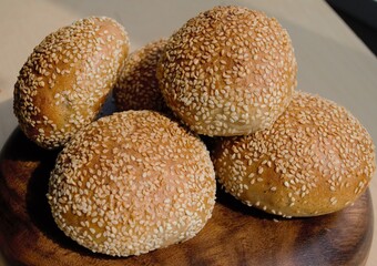 Closeup rye buns with sesame seeds on a dark wood plate. In the daylight