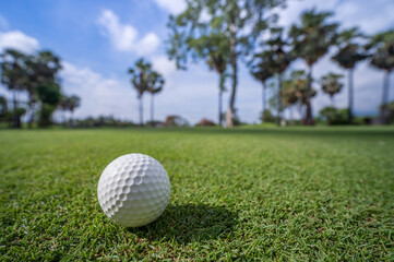 Close-up golf ball on green grass in soft focus at sunlight.