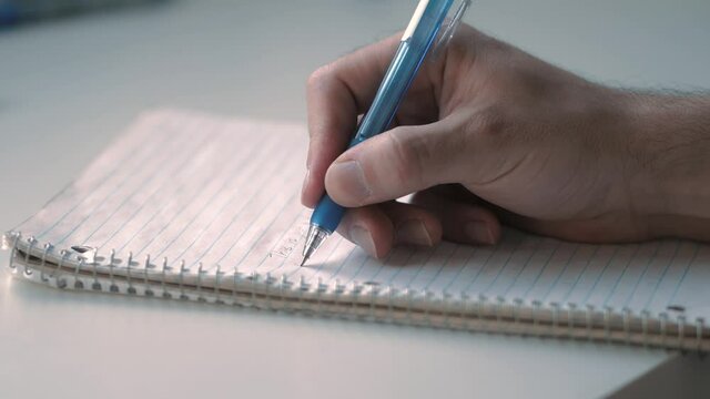 Closeup of a hand of a man writing down notes in a notebook using a pen.