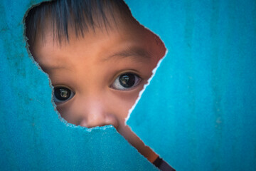 portrait of young small autistic child face looking through cracked blue plastic wall background 