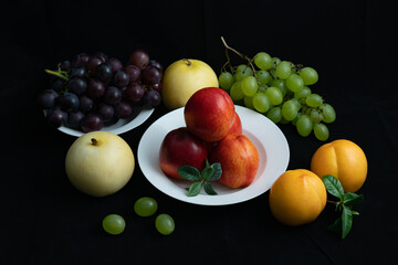 Various fresh fruits on black background.Red nectarine in white dish and yellow peach on black background