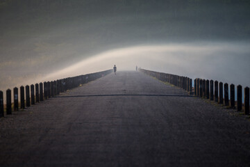 Silhouette of man walking on long road with morning fog 