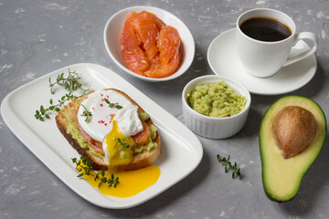 Poached egg with smoked salmon, avocado, toasted bread and coffee  on a white plate.
