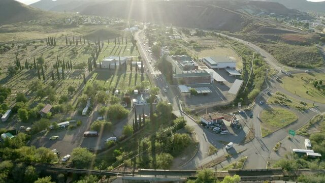 Aerial shot of vehicles on road in city during sunny day, drone flying forward over buildings amidst trees - Bisbee, Arizona