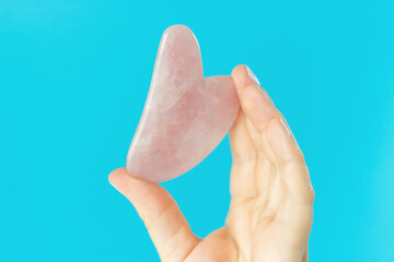 Pink quart guasha in a woman's hand on blue background a copy space