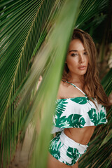 Young caucasian woman near green leaves of palm tree bright makeup portrait lok at the camera