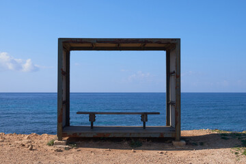 a wooden frame as sun shield with an empty bench towards th sea Paphos Cyprus