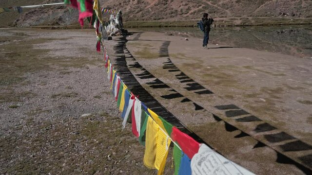 Moving shot of a man framed through prayer flags  clicking pictures at chandratal lake , spiti valley
