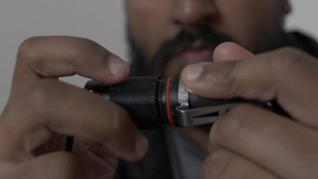 Close Up Of Hands Unscrewing On Battery Cap On Portable LED Torch To Reveal Battery. Low Angle