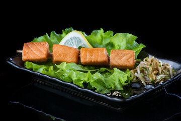 meat on wooden skewers, pork, chicken, fish, scallop, beef, shrimp in a black plate on a black background.