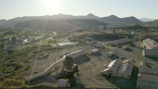 Aerial shot of vehicles on road by buildings against sky on sunny day, drone flying over city near mountains - Bisbee, Arizona