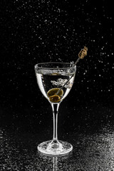 Fresh alcoholic cocktail with vodka and olive in wineglass on black background. Studio shot of drink in freeze motion, flying drops. Summer cold drink and cocktail