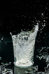 Fresh alcoholic cocktail with vodka, ice, rosemary in glass on black background. Studio shot of drink in freeze motion, flying ice and drops, liquid splash. Summer cold drink and cocktail