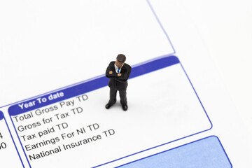 Miniature scale model businessman standing on a wage pay slip showing earnings deductions.  Isolated on a white background