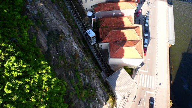 Tilt down shot of funicular moving by houses near river in city on sunny day - Porto, Portugal