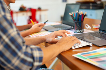 Close-up of two professional designers working on a laptop at an office desk.