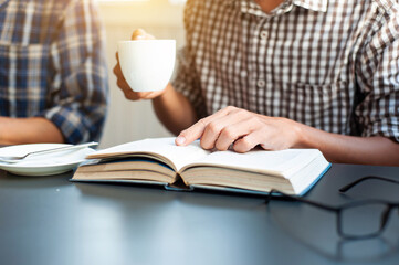 Close-up of a young man drinking coffee while reading on a desk.