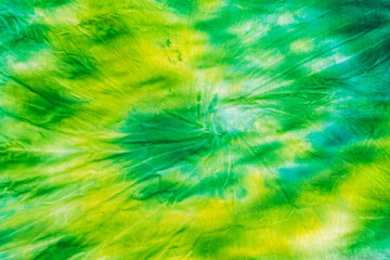 Yellow green spiral tie dye background on fabric. Flat lay.