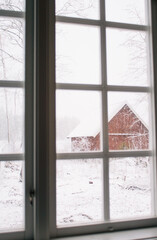 Typical red barn in the winter, view through the window, rural scene in Sweden