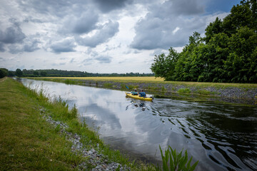 2 canoeists sitting in a canoe and paddling on a canal