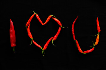 Various red chili and cayenne peppers in black background and love heart shape