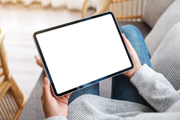 Mockup image of a woman holding black tablet pc with blank desktop white screen while lying on a...