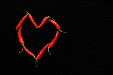 Various red chili and cayenne peppers in black background and love heart shape