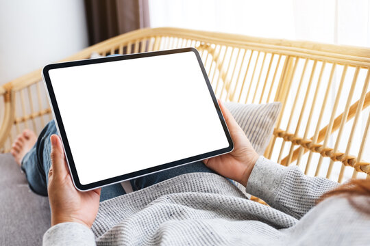 Mockup image of a woman holding black tablet pc with blank desktop white screen while lying on a sofa at home