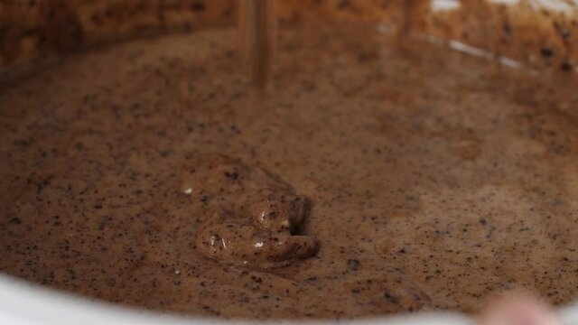 Stir batter for chocolate cake with spatula in white bowl, dripping drops. Macro shot