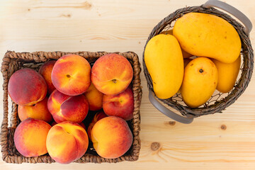Peaches and mangoes in baskets close up on wooden background, view from above