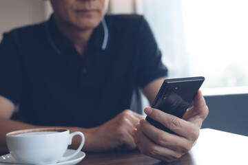 Asian man using mobile phone reading online news in coffee shop