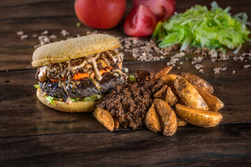 Hambúrguer de carne com cheddar e porção de batata rústica sobre mesa de madeira