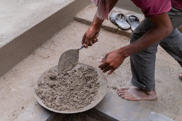 Indian labour mixing cement manually on bucket using trowel with bare hands. Stcok image.