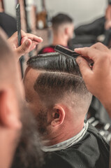 Barbeiro cortando cabelo do seu cliente da sua barbearia no estilo vintage, usando tesoura e navalha e máquina de cortar barbeador elétrico e pente