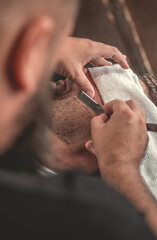 Barbeiro fazendo a barba do seu cliente na sua barbearia, imagem de close no rosto usando navalha