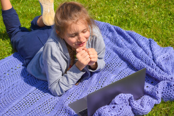 Girl teenager watching lessons on a laptop on the grass. Remote online training.