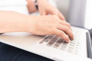 Close up of Asian man hands and fingers using laptop computer working from home sitting on bed, digital lifestyle, work from home concept