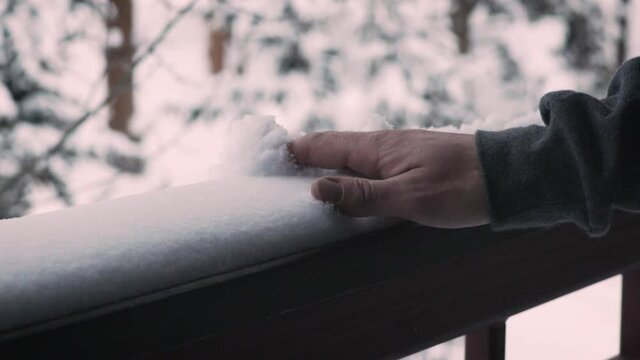 Caucasian male hand brushing and grabbing untouched pristine white snow on railing in slow motion in forest cabin deck