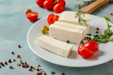 Tasty feta cheese with olives, tomato and spices on color background