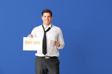 Young businessman holding paper with text DAY OFF and drinking coffee against color background