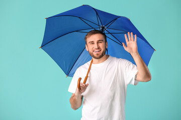 Handsome young man with umbrella on color background
