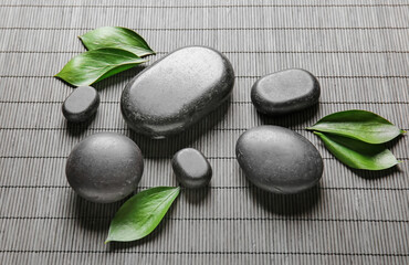 Spa stones and tropical leaves on bamboo mat