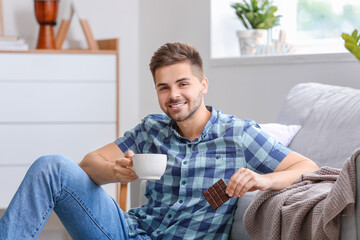 Handsome young man with tasty chocolate and cup of tea at home