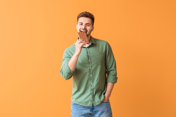Handsome young man with tasty chocolate on color background