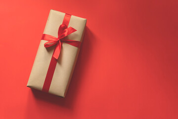 present box wrapped in plain paper with a red ribbon on red background